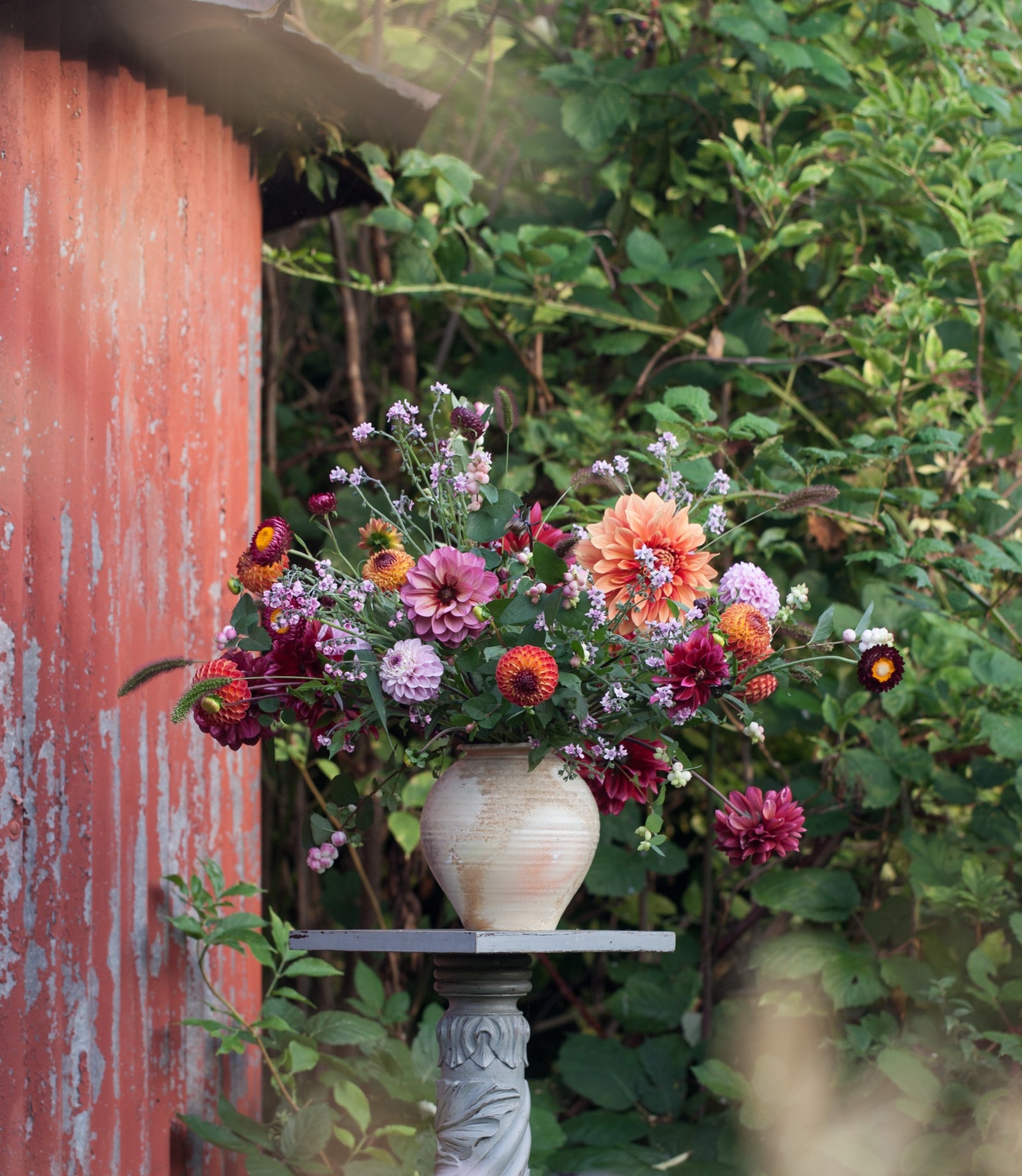 An autumn arrangement of garden flowers in a vase against a red timber wall